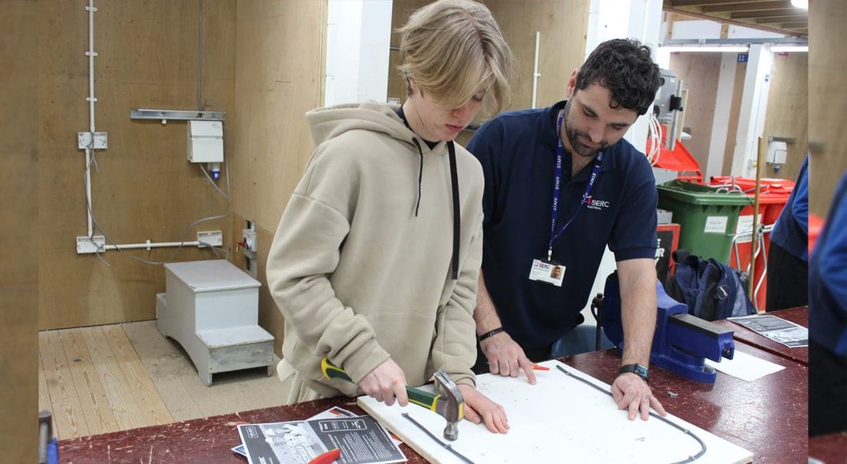 aspiring electrician practicing skills with lecturer looking on